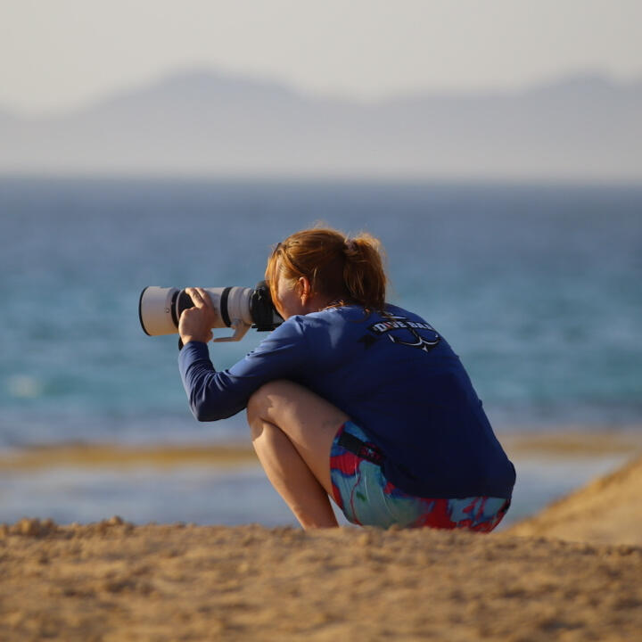 Adventure Photographer at Work | Savanna Goodman Savanna Goodman photographing beside the ocean with a professional camera and telephoto lens